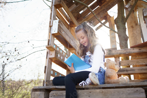 Girl sitting in garden at tree house and writing something in her blue diary photo