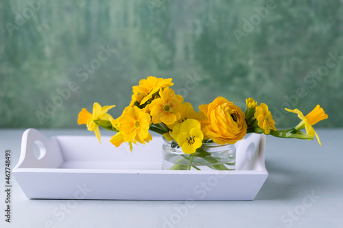 Persian buttercup, daffodil, primrose and horned violet in glass on wooden tray photo