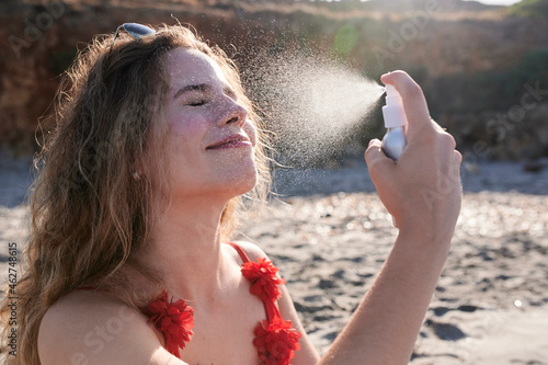 Young woman applying suncream spray on the beach photo