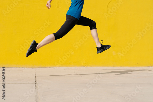 Young woman jogging in front of a yellow wall photo