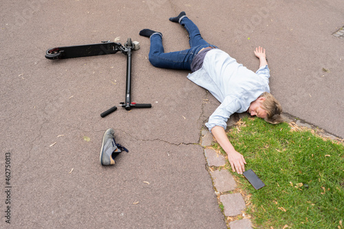 Accident victim lying on road besides E-Scooter and smartphone photo