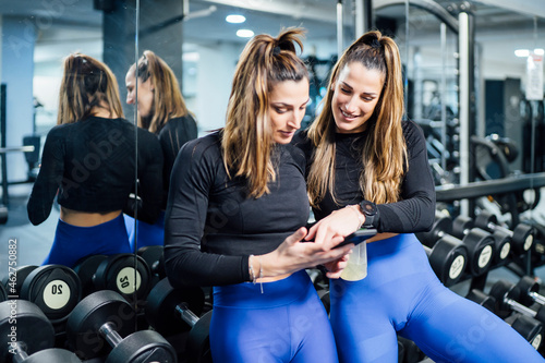 Twin sisters having a break in gym using smartphone photo