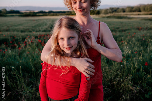 Mother stroking daughte's hair, standing in a poppy field photo