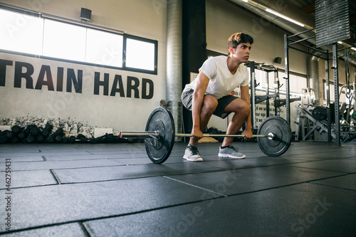 Male athlete lifting deadlift while exercising in gym photo