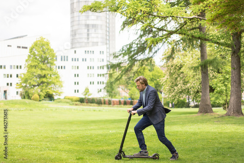 Businessman using E-Scooter on a meadow in city park, Essen, Germany photo