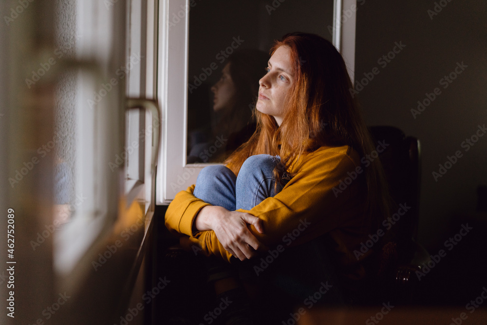 Pensive redheaded woman sitting at open window looking at distance Pensive redheaded woman sitting at open window looking at distance