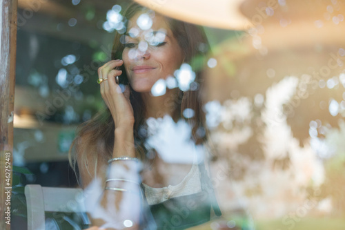 Young woman on cell phone behind windowpane of a cafe