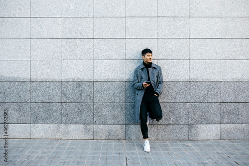Young man with mobile phone leaning against wall waiting