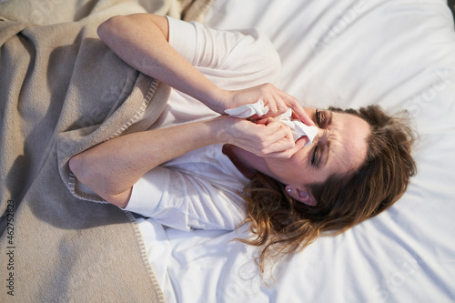 Woman lying in bed blowing her nose photo