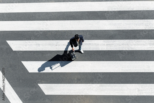 Man on zebra crossing pushing his trolley bag, top view