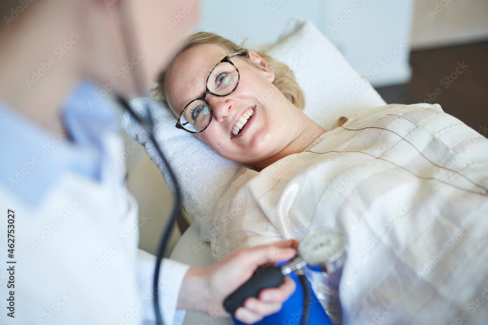 Smiling patient looking at doctor taking blood pressure in medical practice Smiling patient looking at doctor taking blood pressure in medical practice
