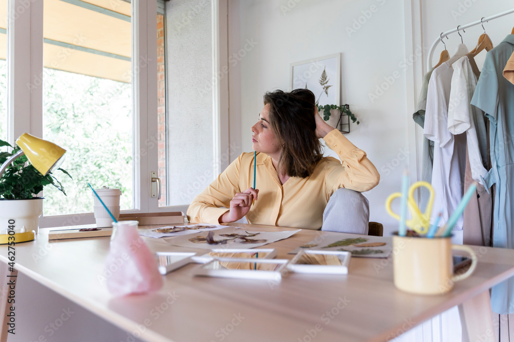 Thoughtful woman looking away sitting at table with decoration material Thoughtful woman looking away sitting at table with decoration material