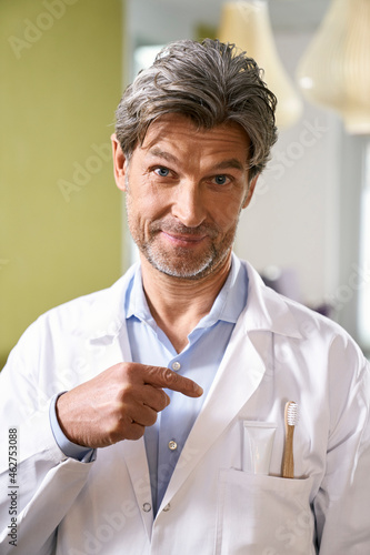 Portrait of dentist pointing at toothbrush in his pocket photo