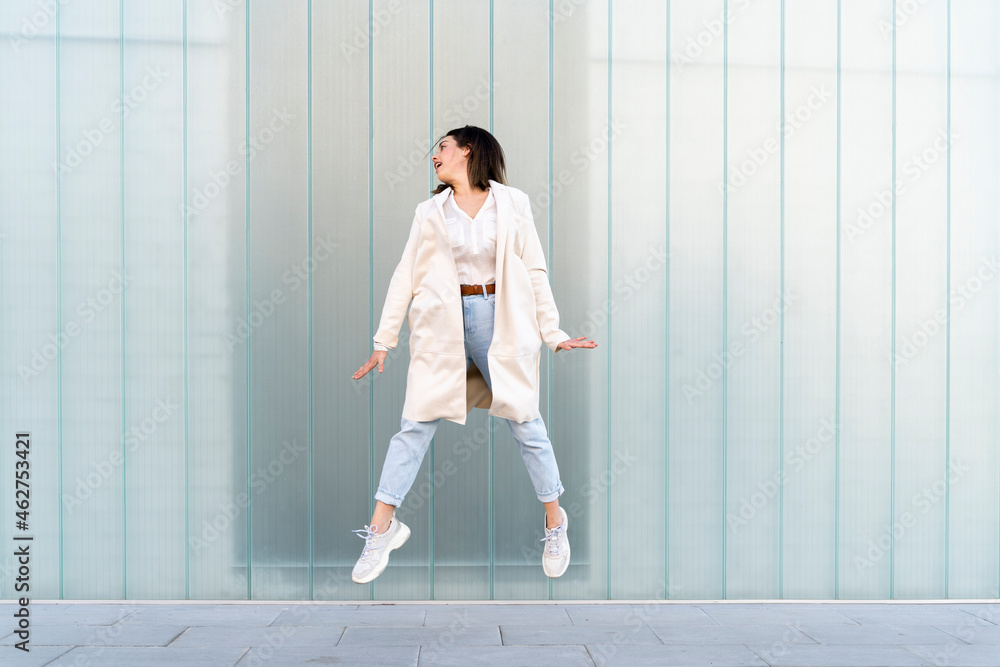Female entrepreneur jumping in mid-air against glass wall Female entrepreneur jumping in mid-air against glass wall