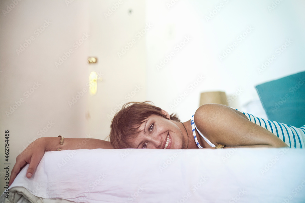 Smiling young woman lying on bed at home Smiling young woman lying on bed at home