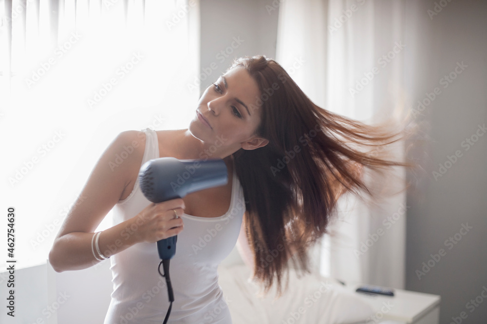 Young woman drying hair while standing in bedroom at home Young woman drying hair while standing in bedroom at home