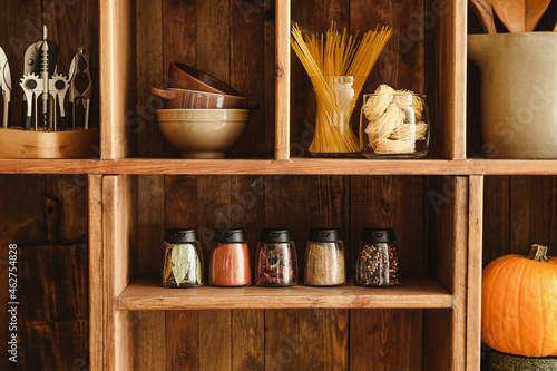 Jars with different spices, raw pasta and kitchen utensils on shelves