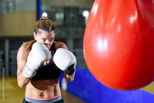 Female boxer training at punch bag in gym photo