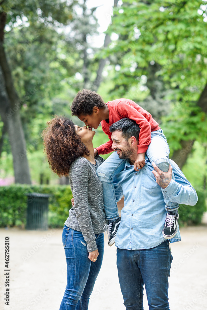 Father carrying son piggyback in a park, while son is kissing his mother Father carrying son piggyback in a park, while son is kissing his mother