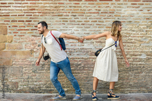 Couple holding hands walking in opposite directions at brick wall