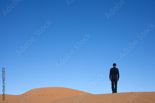 Morocco, Merzouga, Erg Chebbi, rear view of man wearing a bowler hat standing on desert dune