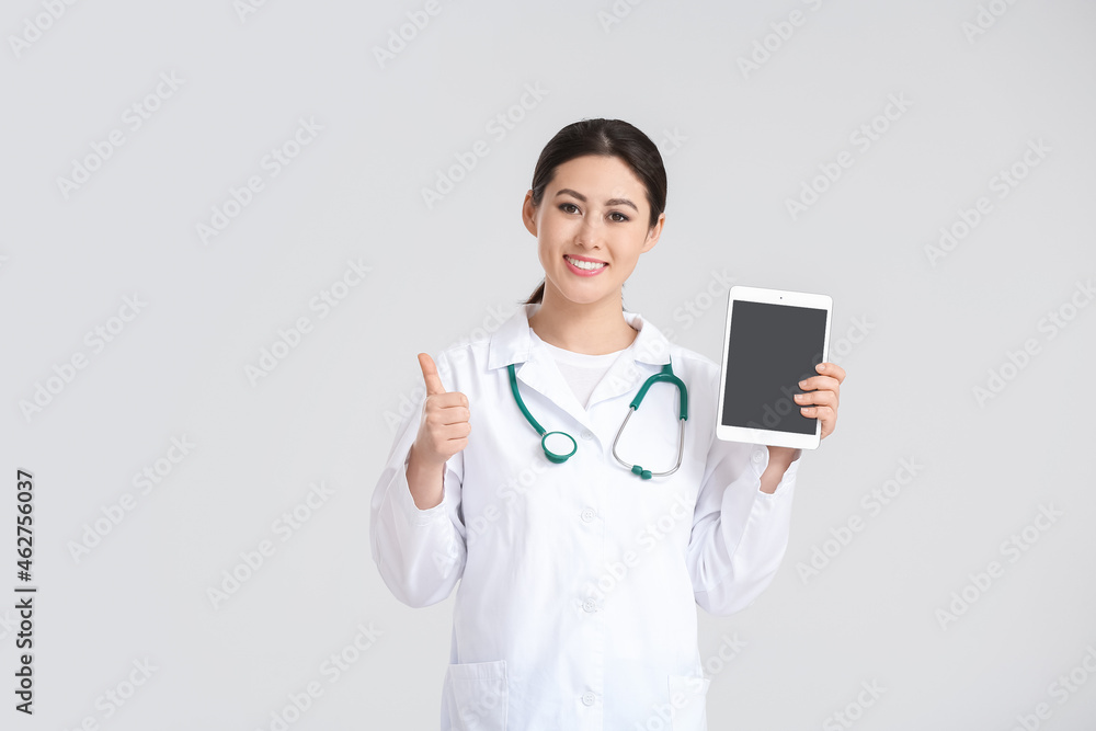 Portrait of female Asian doctor with tablet showing thumb-up on light background Portrait of female Asian doctor with tablet showing thumb-up on light background