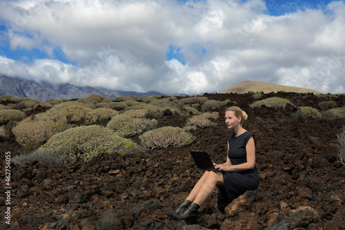Spain, Tenerife, Malpais de Guimar, woman sitting in volcanic landscape with cacti using laptop photo