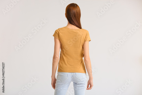 Young woman in modern t-shirt on light background, back view