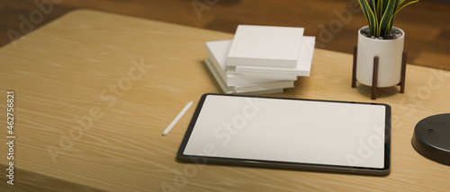 Tablet computer blank screen mockup with books, stylus pen and plant on wooden table