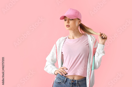 Woman in baseball cap touching hair on pink background photo