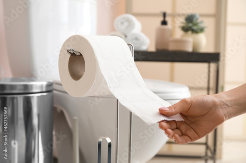 Photos Woman tearing off toilet paper in modern bathroom