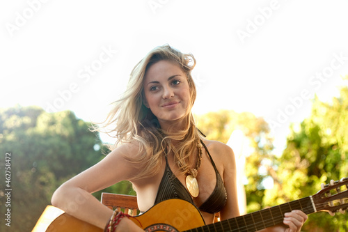 Smiling young woman playing guitar in bikini at beach
