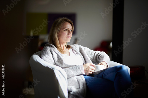 Woman sitting at home, relaxing in arm chair photo