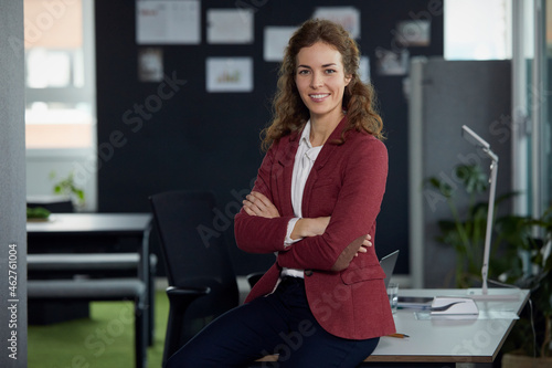 Portrait of confident businesswoman sitting on desk in office photo