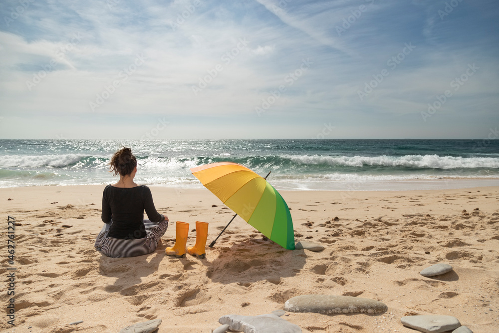 Woman with colorful umbrella sitting on the beach, rear view