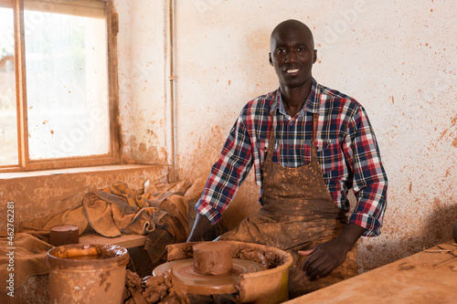 Portrait of positive afro man making ceramic pot on pottery wheel