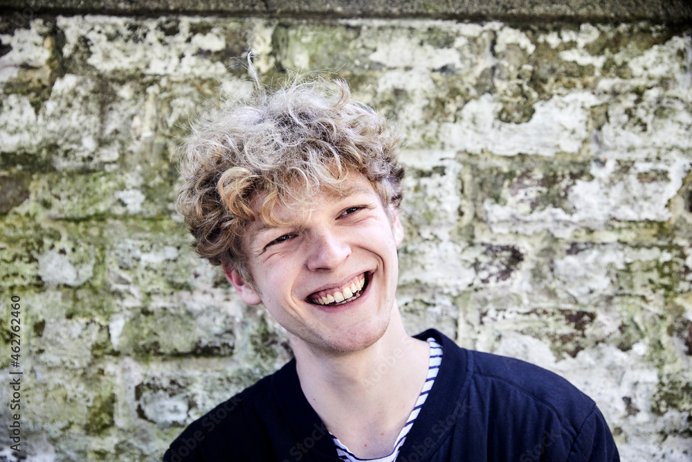 Portrait of laughing young man with curly blond hair in front of weathered wall Portrait of laughing young man with curly blond hair in front of weathered wall