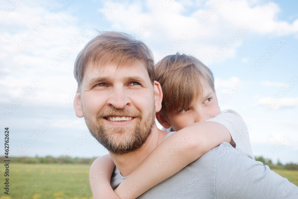 Smiling man giving son piggyback against sky Smiling man giving son piggyback against sky
