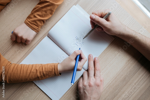 Top view of father and son scribbling into notebook on table