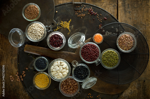 Jars and bowls with various beans and lentils on rustic baking sheet photo