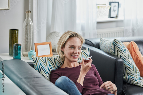 Smiling young woman using cell phone lying on couch at home photo