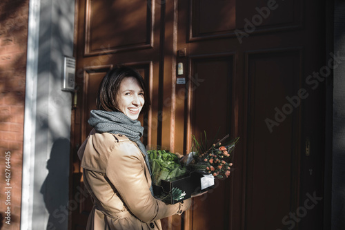 Portrait of laughing woman with cardboard box of purchases standing in front of house entrance photo