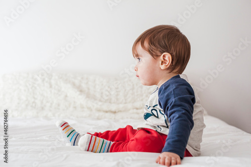 Side view of baby boy sitting on bed looking at distance photo