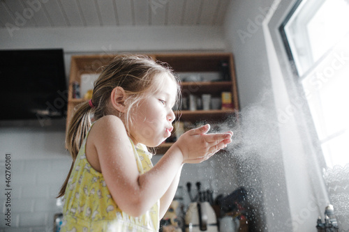 Little girl blowing flour in the air in the kitchen