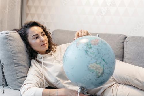 Portrait of woman lying on the couch at home looking at globe photo