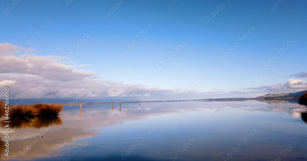 Time Lapse - Vast serene lake and blue sky mirrored, as clouds and breeze arrive Time Lapse - Vast serene lake and blue sky mirrored, as clouds and breeze arrive