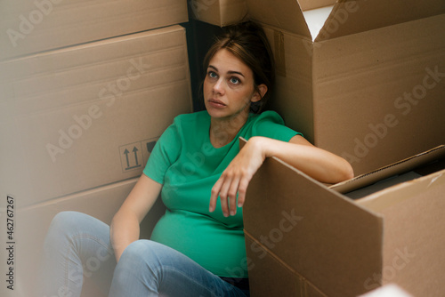 Exhausted pregnant woman sitting on floor surrounded by cardboard boxes photo