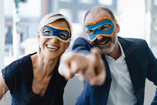 Businessman and woman wearing super hero masks, pointing at camera photo