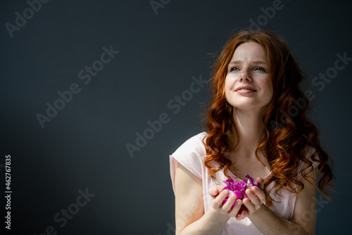 Portrait of redheaded woman with hadful of purple orchid blossoms