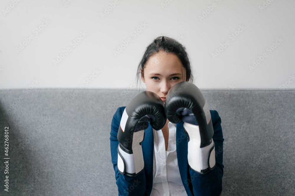 Portrait of young woman on couch wearing boxing gloves Portrait of young woman on couch wearing boxing gloves